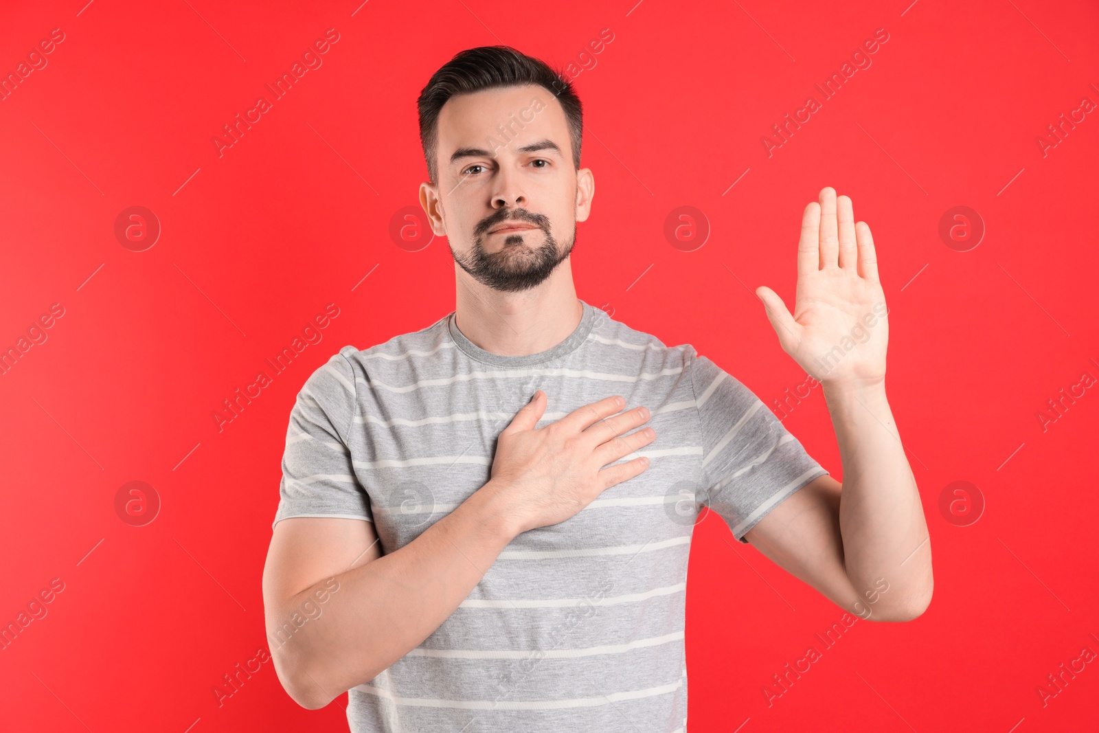 Photo of Man making promise with raised hand on red background. Oath gesture