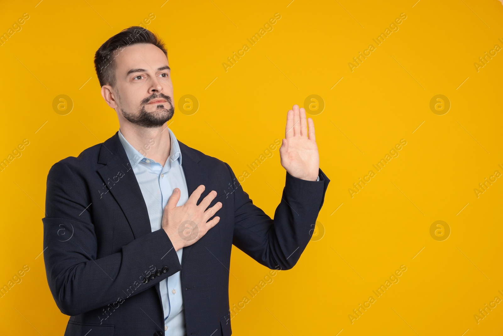 Photo of Man making promise with raised hand on orange background, space for text. Oath gesture