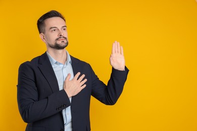 Photo of Man making promise with raised hand on orange background, space for text. Oath gesture