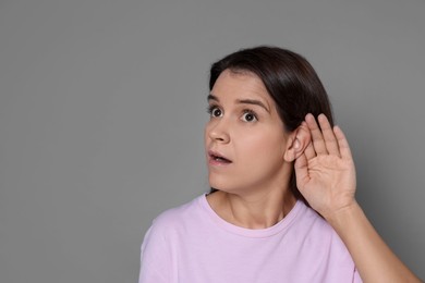 Photo of Woman showing hand to ear gesture on grey background, space for text