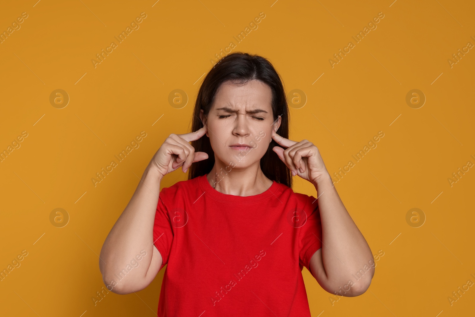 Photo of Woman covering her ears with fingers on orange background