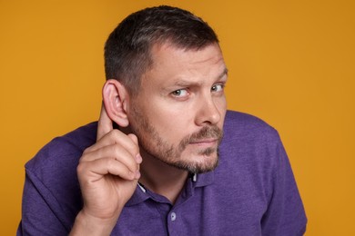 Photo of Man showing hand to ear gesture on orange background