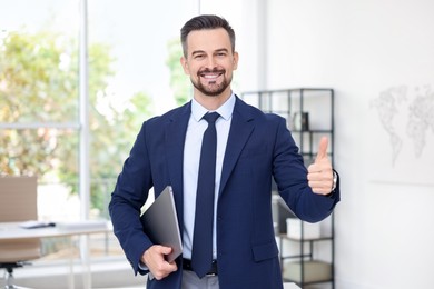 Photo of Portrait of smiling banker with laptop showing thumbs up in office