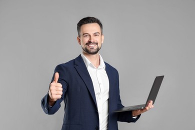 Photo of Portrait of smiling banker with laptop showing thumbs up on grey background