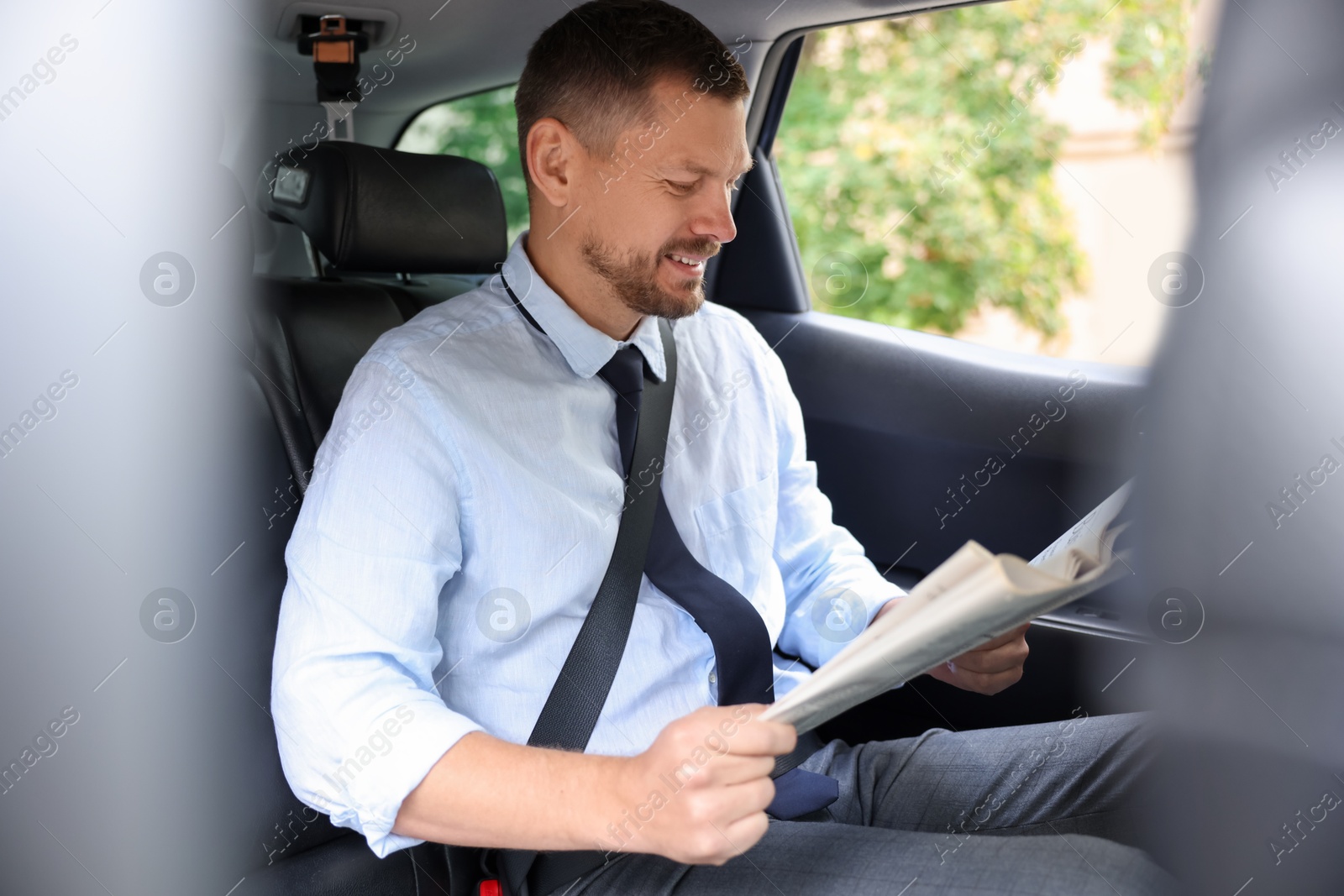 Photo of Handsome man reading newspaper in modern car