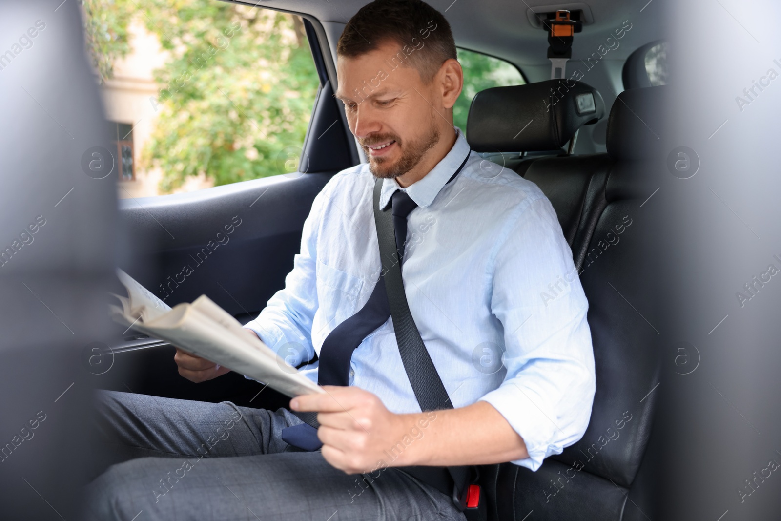 Photo of Handsome man reading newspaper in modern car