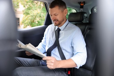 Photo of Handsome man reading newspaper in modern car