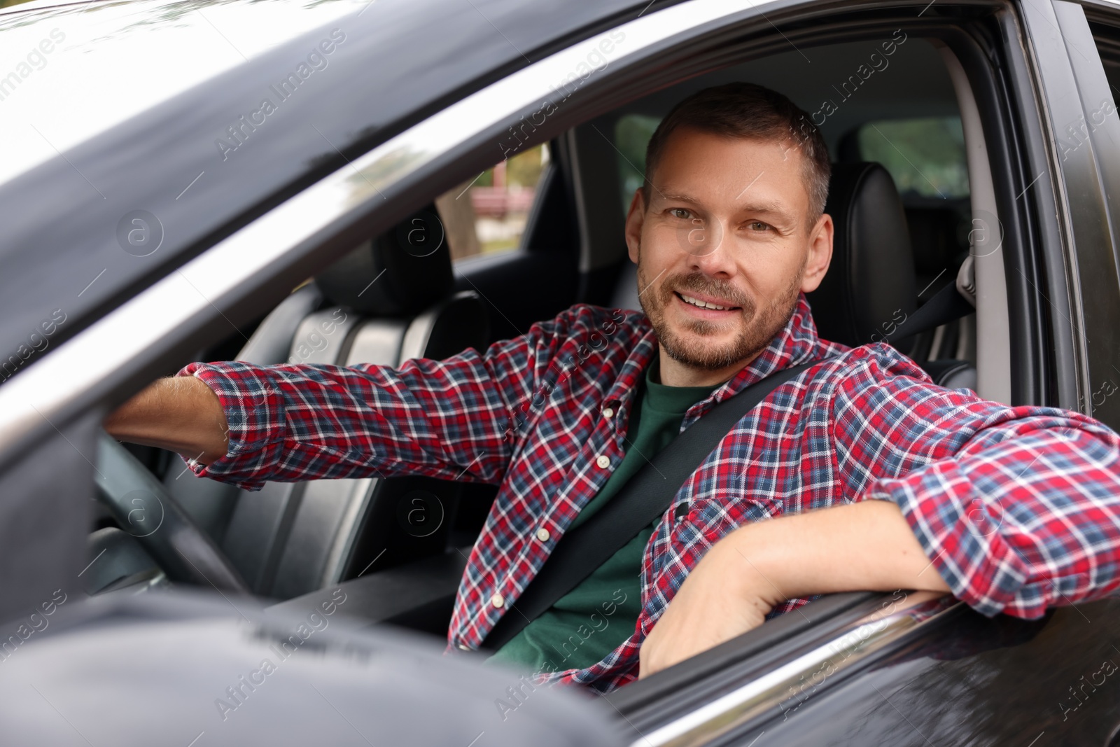 Photo of Happy man behind steering wheel of modern car, view from outside