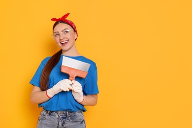 Photo of Portrait of young decorator with putty knife on orange background, space for text