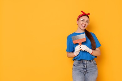 Photo of Portrait of young decorator with putty knife on orange background, space for text