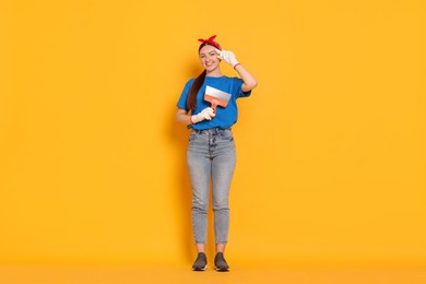 Photo of Young decorator with putty knife on orange background