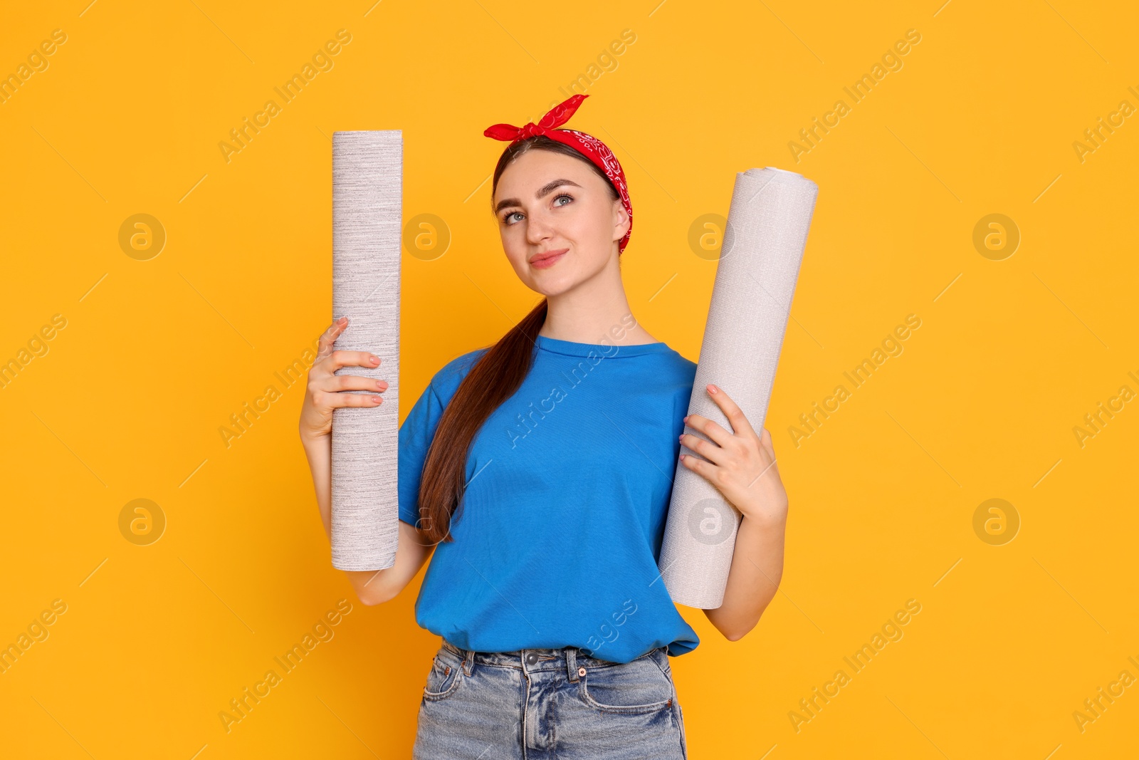 Photo of Young decorator with rolls of wallpaper on orange background