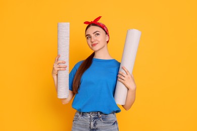 Photo of Young decorator with rolls of wallpaper on orange background