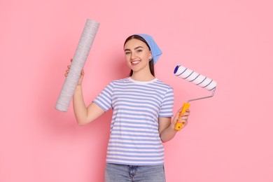 Photo of Young decorator with paint roller and roll of wallpaper on pink background