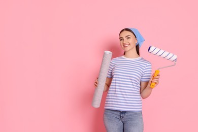 Photo of Young decorator with paint roller and roll of wallpaper on pink background, space for text