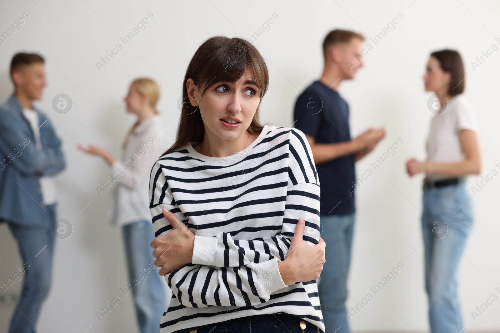 Photo of Young woman feeling uncomfortable among people indoors, selective focus