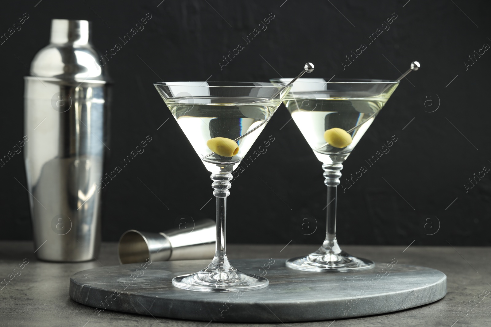 Photo of Martini cocktail with olives in glasses on grey table against black background