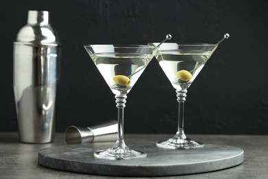 Photo of Martini cocktail with olives in glasses on grey table against black background