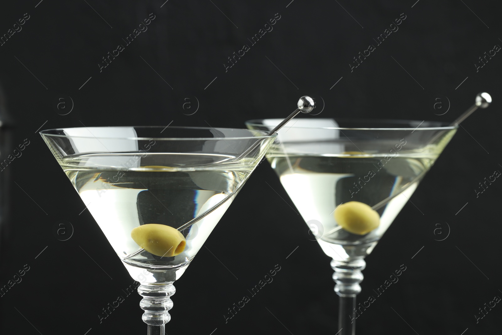 Photo of Martini cocktail with olives in glasses on black background, closeup