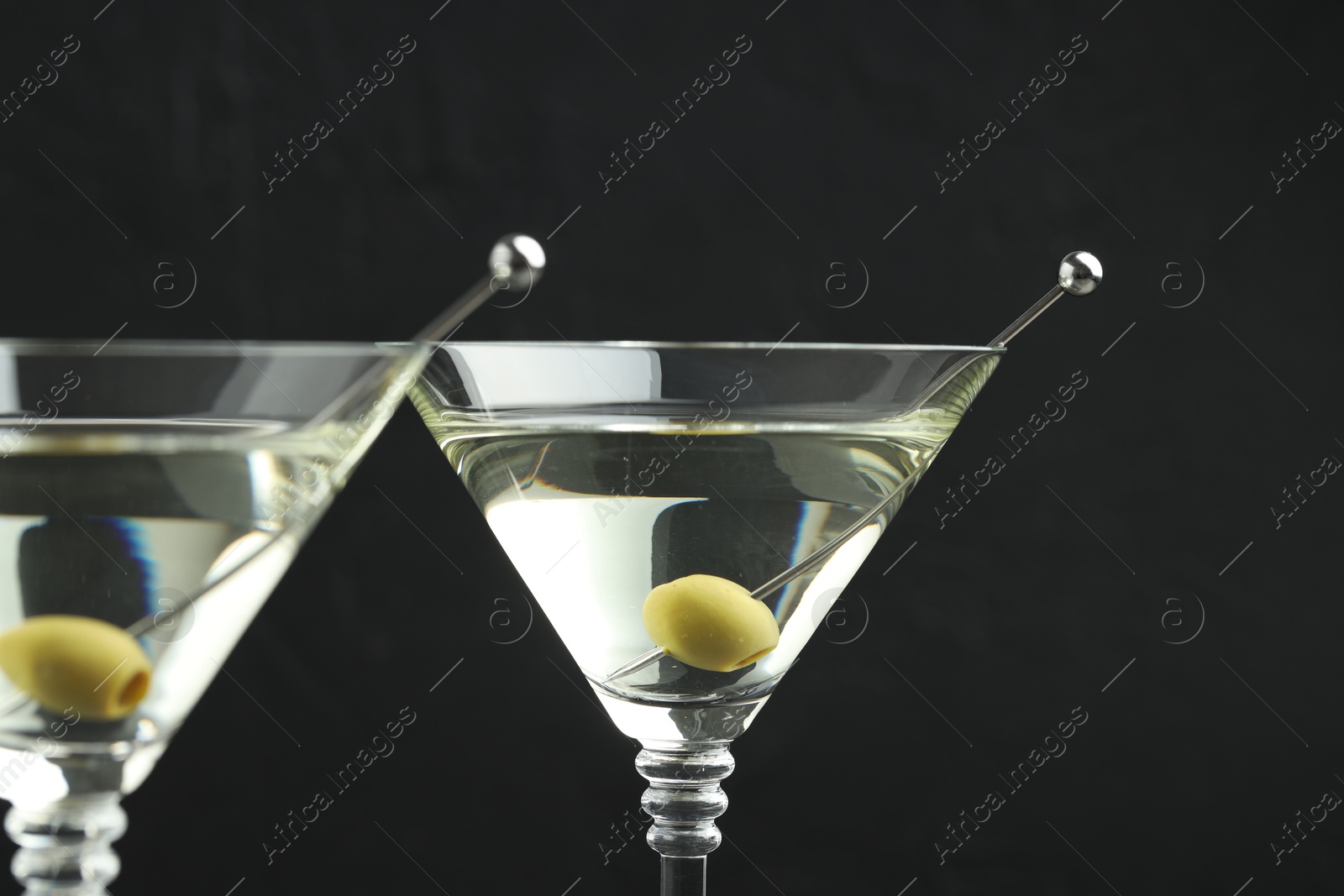 Photo of Martini cocktail with olives in glasses on black background, closeup