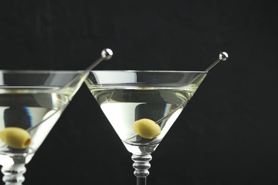 Photo of Martini cocktail with olives in glasses on black background, closeup