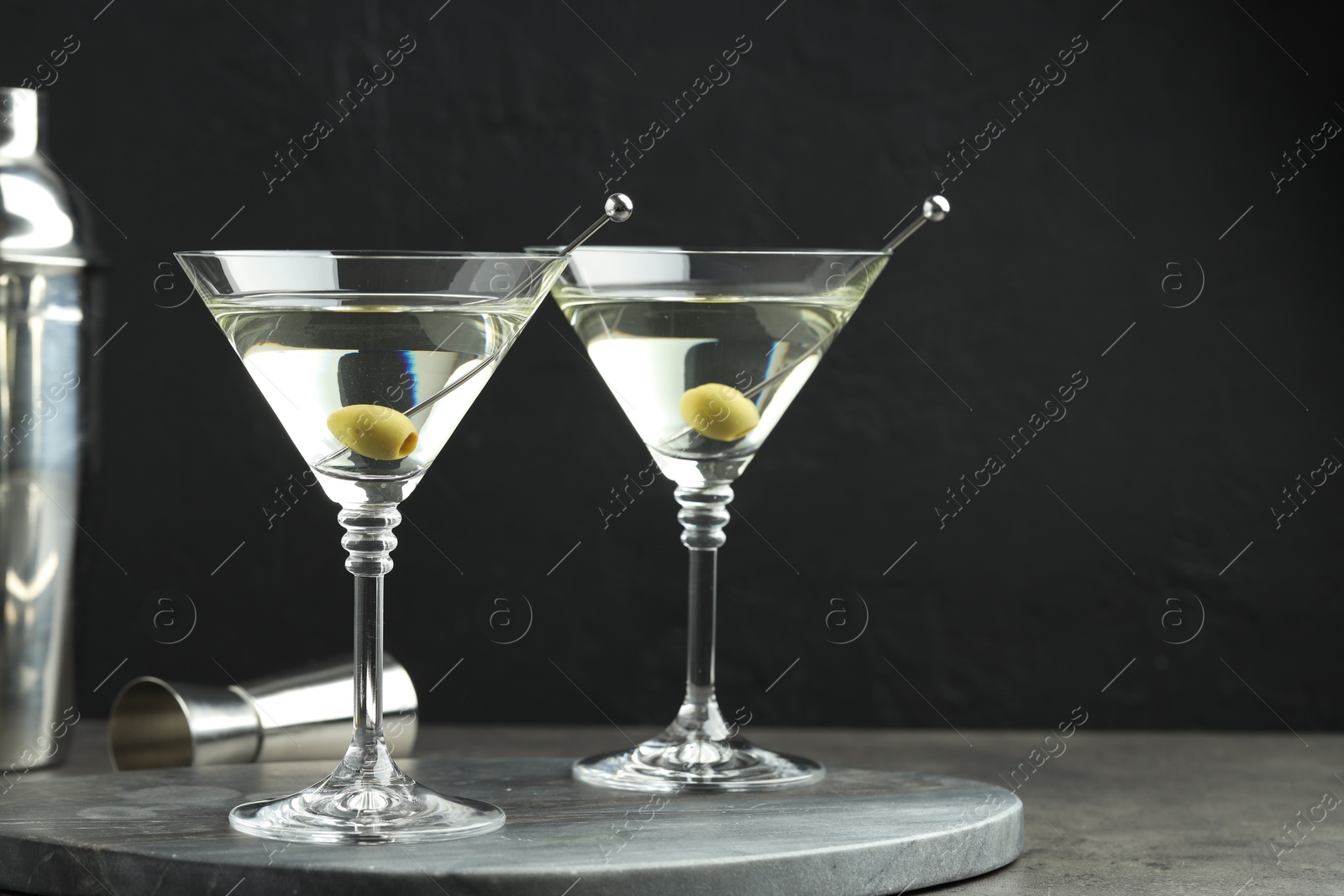 Photo of Martini cocktail with olives in glasses on grey table against black background