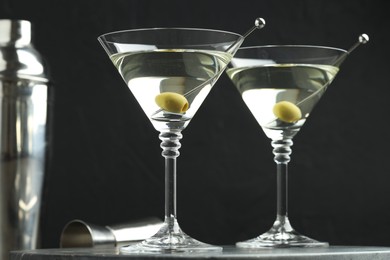 Photo of Martini cocktail with olives in glasses on grey table against black background, closeup