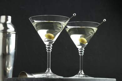 Photo of Martini cocktail with olives in glasses on grey table against black background, closeup