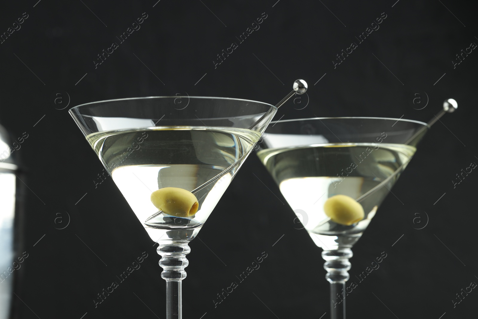 Photo of Martini cocktail with olives in glasses on black background, closeup