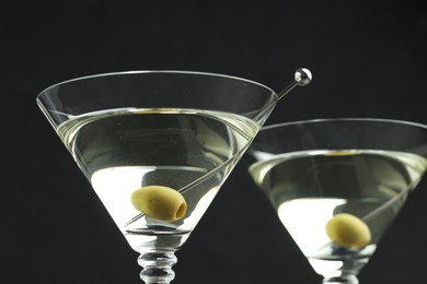 Photo of Martini cocktail with olives in glasses on black background, closeup