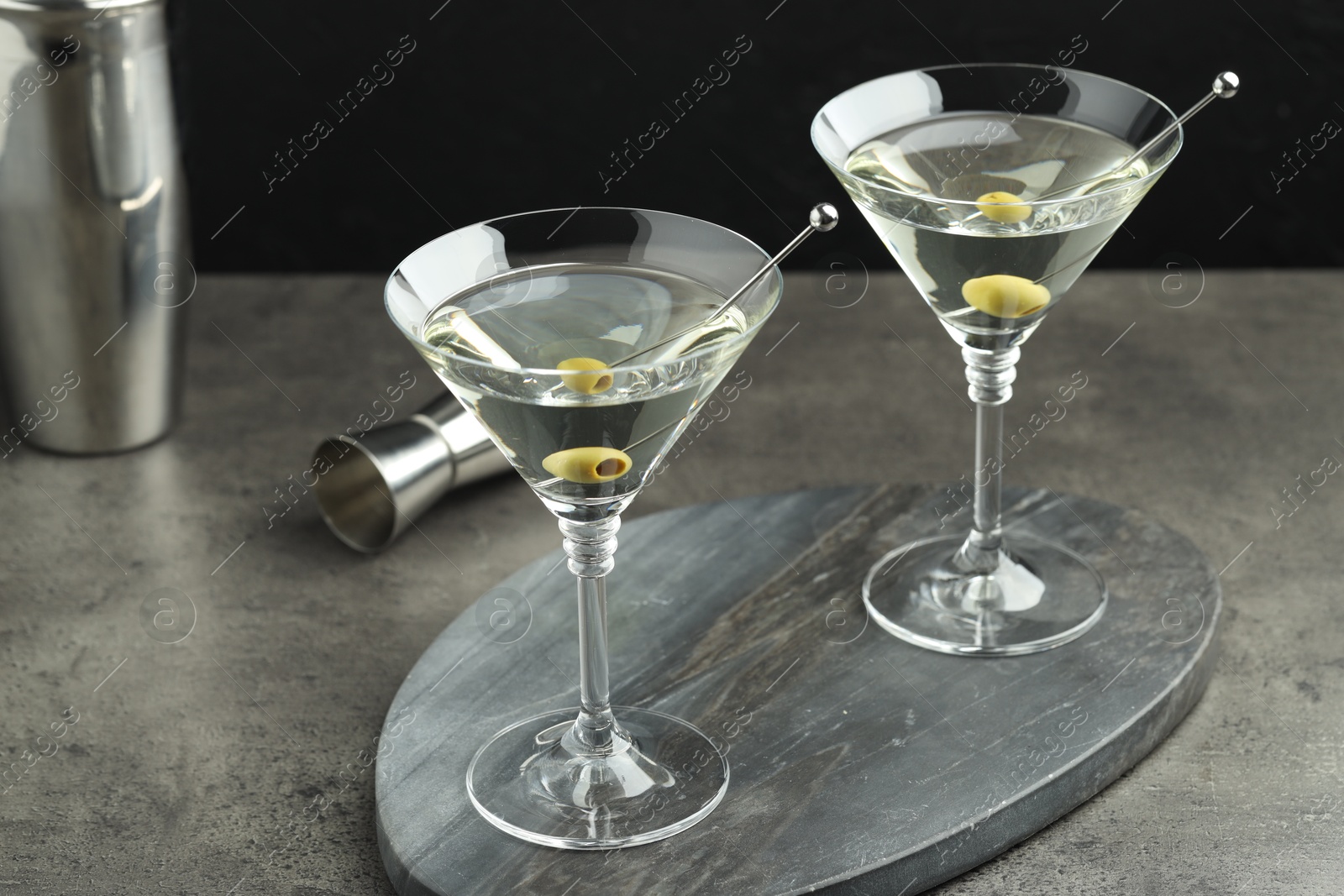 Photo of Martini cocktail with olives in glasses on grey table against black background