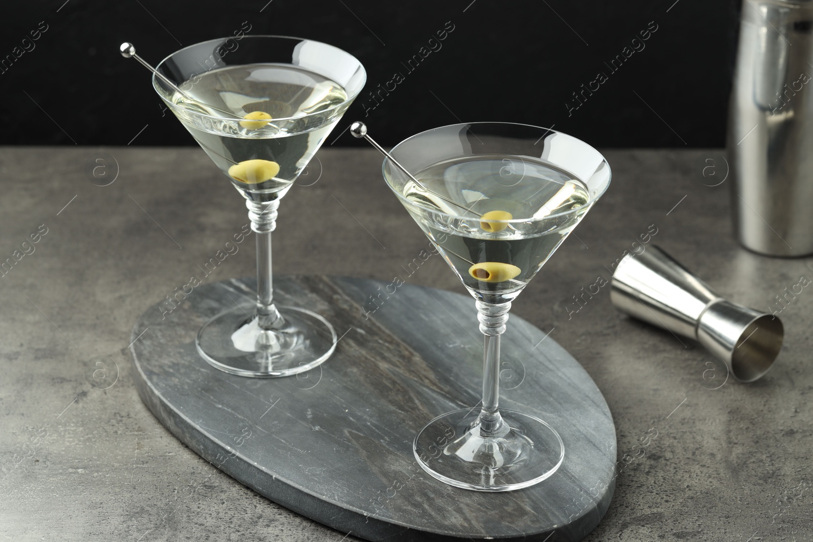 Photo of Martini cocktail with olives in glasses on grey table against black background