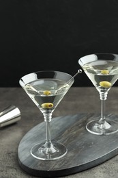 Photo of Martini cocktail with olives in glasses on grey table against black background