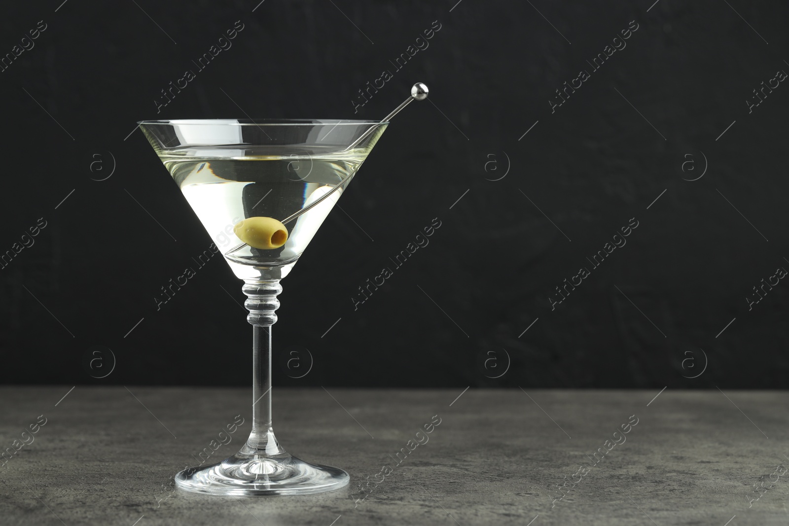 Photo of Martini cocktail with olives in glass on grey table against black background, space for text