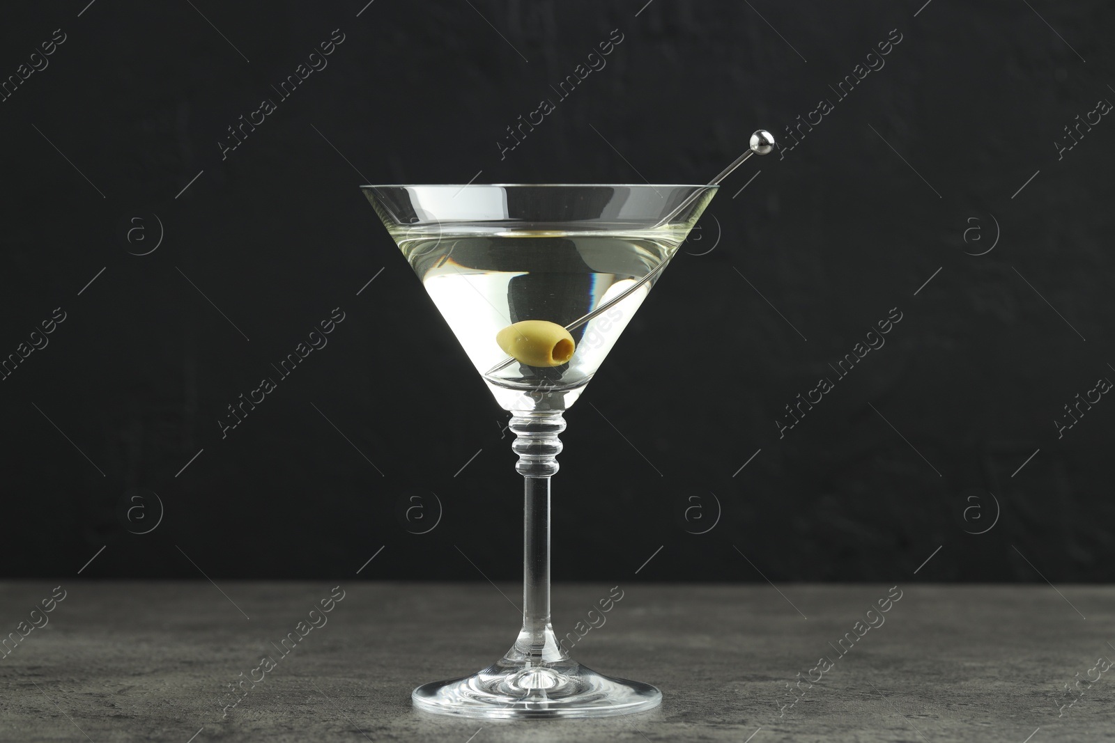 Photo of Martini cocktail with olives in glass on grey table against black background