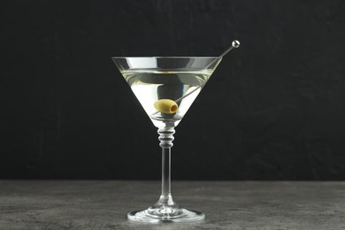 Photo of Martini cocktail with olives in glass on grey table against black background