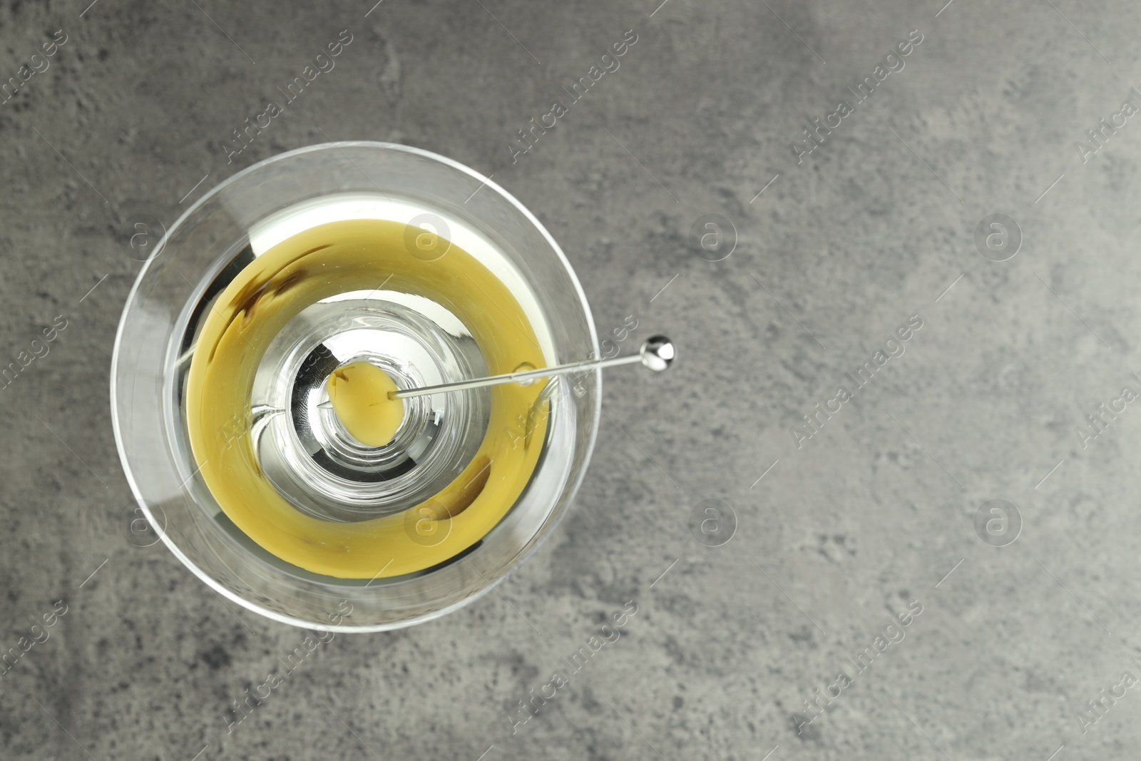 Photo of Martini cocktail with olive in glass on grey table, top view. Space for text