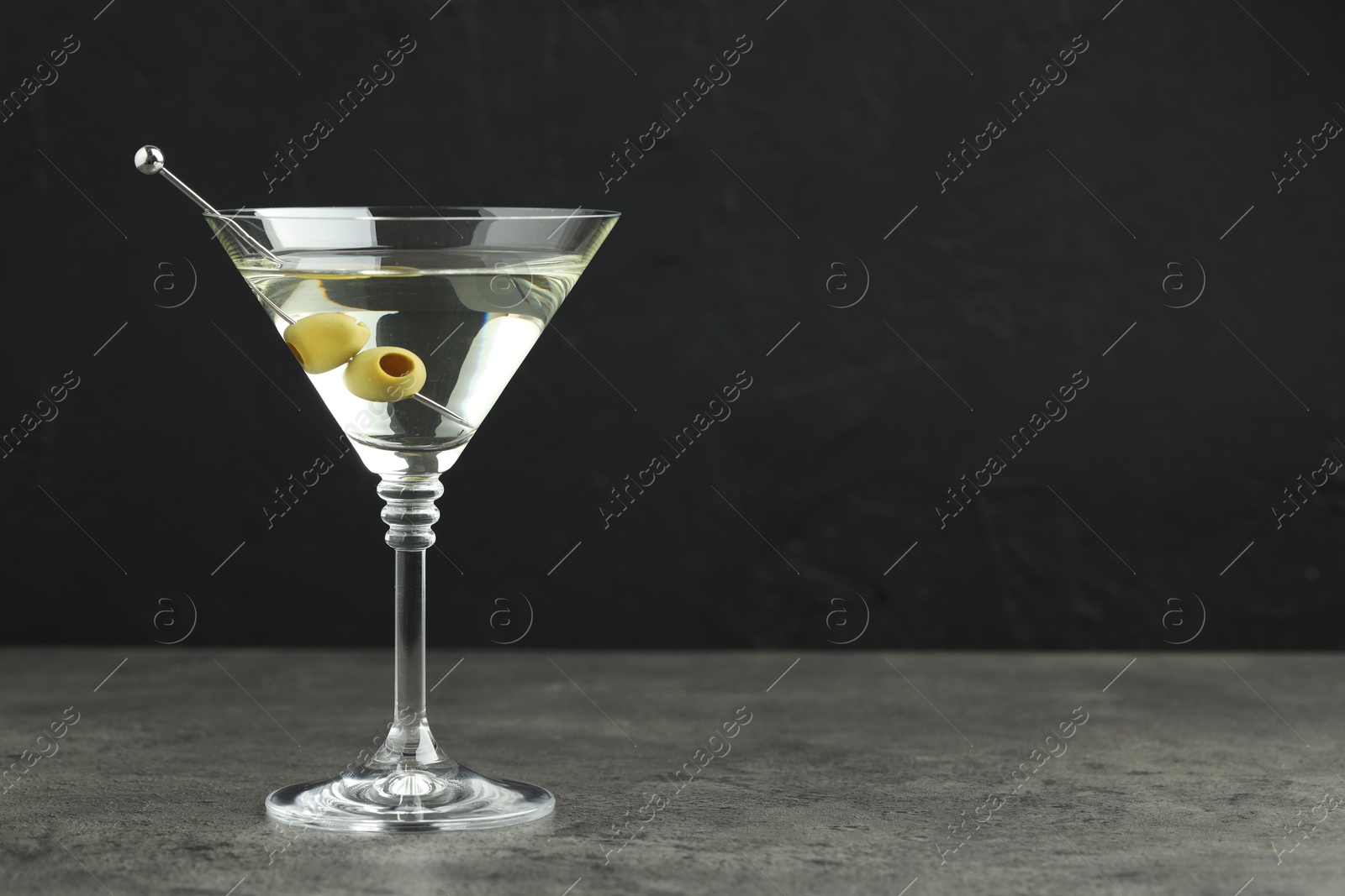 Photo of Martini cocktail with olives in glass on grey table against black background, space for text