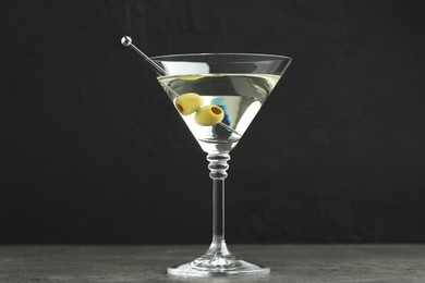 Photo of Martini cocktail with olives in glass on grey table against black background