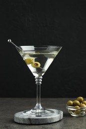 Photo of Martini cocktail with olives in glass on grey table against black background