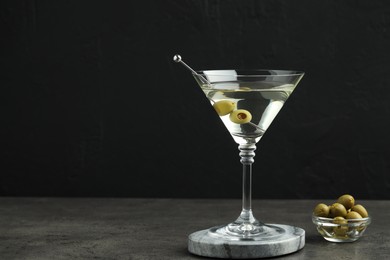 Photo of Martini cocktail with olives in glass on grey table against black background, space for text