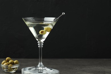 Photo of Martini cocktail with olives in glass on grey table against black background, space for text