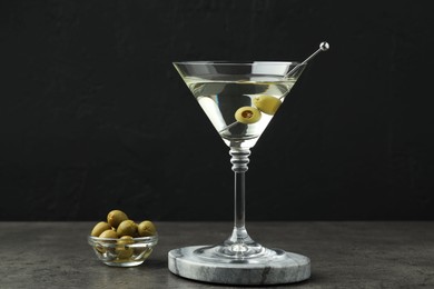 Photo of Martini cocktail with olives in glass on grey table against black background