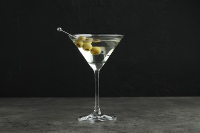 Photo of Martini cocktail with olives in glass on grey table against black background