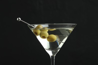 Photo of Martini cocktail with olives in glass on black background, closeup