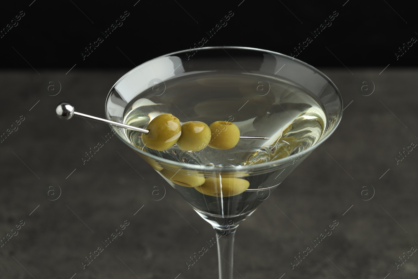 Photo of Martini cocktail with olives in glass on grey table against black background, closeup