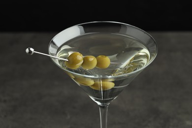 Photo of Martini cocktail with olives in glass on grey table against black background, closeup