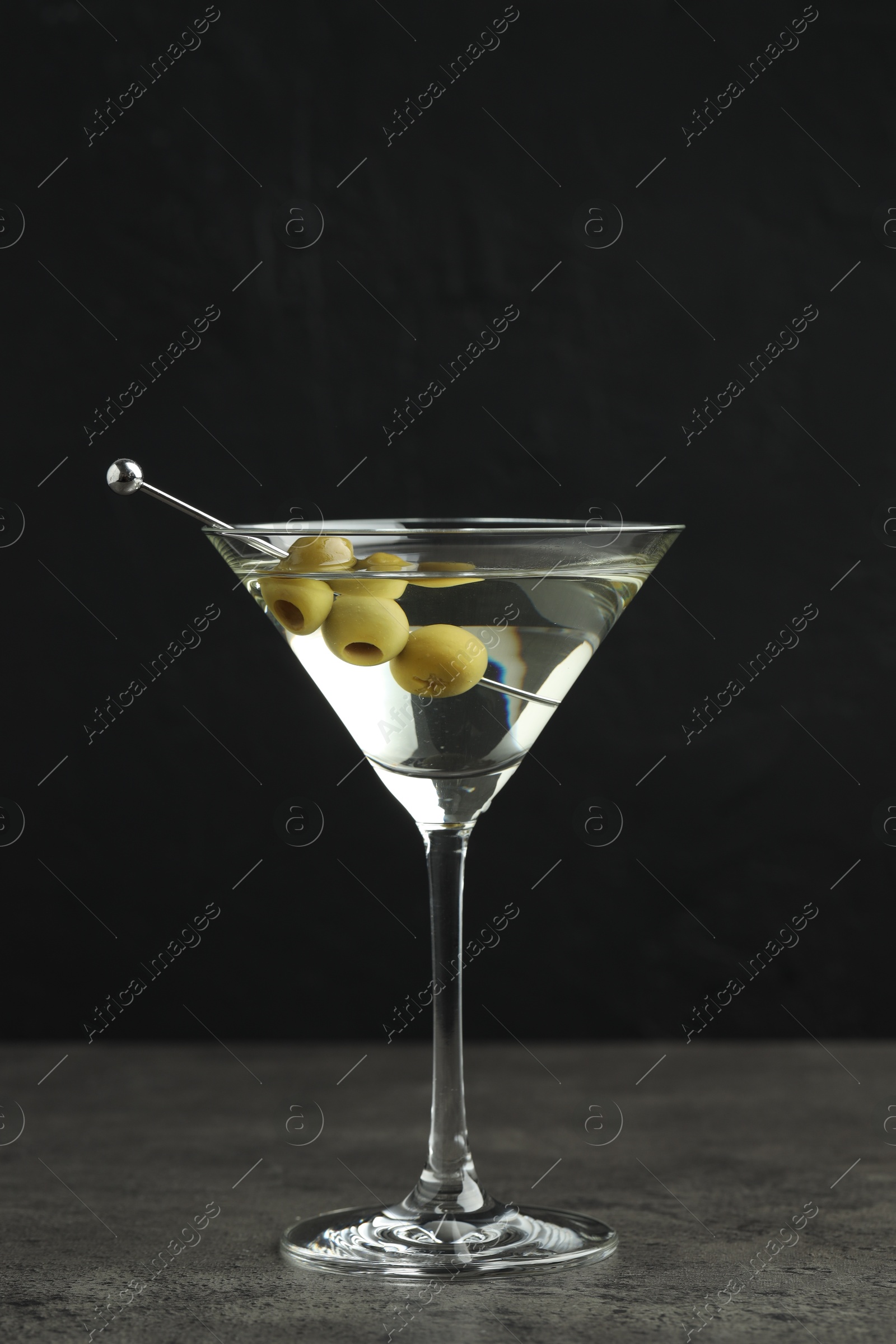 Photo of Martini cocktail with olives in glass on grey table against black background