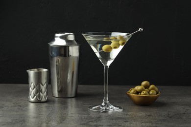 Photo of Martini cocktail with olives in glass and shaker on grey table against black background