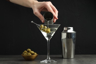 Photo of Woman making martini cocktail with olives on grey table, closeup